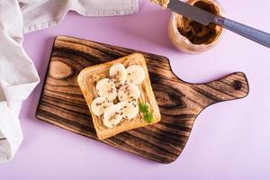 Peanut butter toast with banana, flax seeds and mint on a cutting board. Top view. photo