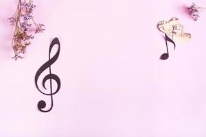 Paper musical clef, notes, hearts and dried flowers on a pink background. Top view. photo