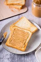 Bread toast with peanut butter on a plate and a jar of butter on the table. Vertical view photo