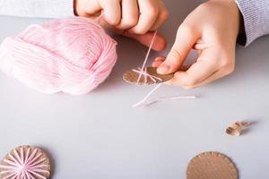 las manos de los niños envuelven hilo alrededor de un círculo de cartón para hacer decoraciones navideñas hechas a mano. foto