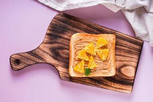 Peanut butter toast with orange, sesame and mint on a cutting board. Top view. photo