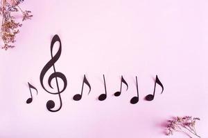 Paper musical clef and notes in a row and dried flowers on a pink background. Top view. photo