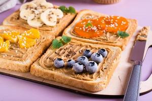 Toast with peanut butter, fruits, berries, flax seeds and sesame seeds on a cutting board. photo