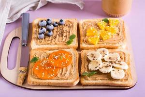 Toast with peanut butter, banana, persimmon, orange, flax seeds and sesame seeds on a cutting board. photo