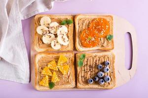 Toast with peanut butter, fruits, berries, flax seeds and sesame seeds on a cutting board. Top view. photo