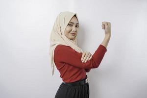 Excited Asian Muslim woman wearing a hijab showing strong gesture by lifting her arms and muscles smiling proudly photo