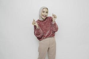 A happy young Asian woman wearing a pink sweater and hijab feels romantic shapes heart gesture expresses tender feelings photo