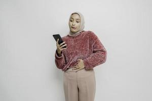 Photo of a hungry excited young woman holding her phone and wondering what to order yummy food isolated on white color background