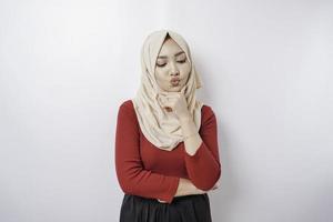 A thoughtful young woman is wearing a hijab and holding her chin isolated by white background photo