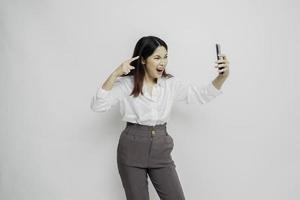 A dissatisfied young Asian woman looks disgruntled wearing white shirt irritated face expressions holding her phone photo