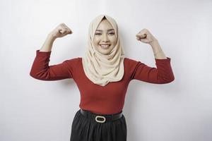 Excited Asian Muslim woman wearing a hijab showing strong gesture by lifting her arms and muscles smiling proudly photo