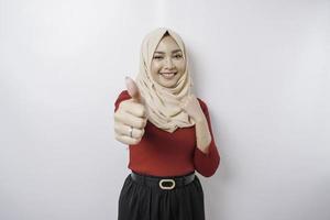 Excited Asian woman wearing a hijab gives thumbs up hand gesture of approval, isolated by white background photo