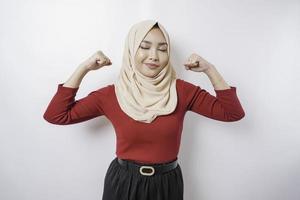 Excited Asian Muslim woman wearing a hijab showing strong gesture by lifting her arms and muscles smiling proudly photo