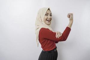 Excited Asian Muslim woman wearing a hijab showing strong gesture by lifting her arms and muscles smiling proudly photo