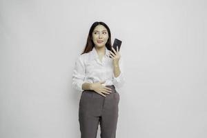 Photo of a hungry excited young woman holding her phone and wondering what to order yummy food isolated on white color background