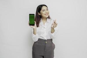 una joven asiática feliz con un pantalones blanco, que muestra un gesto de corazón expresa sentimientos tiernos mientras muestra espacio de copia en su teléfono foto