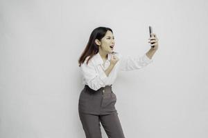 una joven asiática insatisfecha se ve descontenta usando camisa blanca expresiones faciales irritadas sosteniendo su teléfono foto