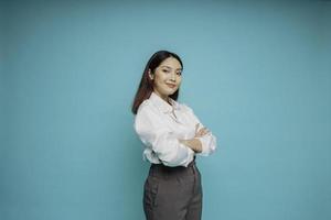 Portrait of a confident smiling Asian woman wearing white shirt standing with arms folded and looking at the camera isolated over blue background photo