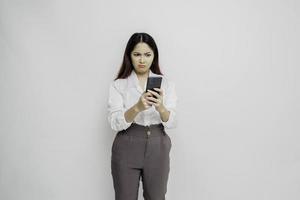 una joven asiática insatisfecha se ve descontenta usando camisa blanca expresiones faciales irritadas sosteniendo su teléfono foto