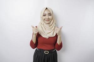 Excited Asian woman wearing a hijab gives thumbs up hand gesture of approval, isolated by white background photo