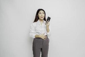 Photo of a hungry excited young woman holding her phone and wondering what to order yummy food isolated on white color background