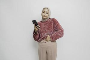 Photo of a hungry excited young woman holding her phone and wondering what to order yummy food isolated on white color background