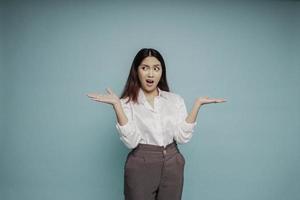 mujer asiática sorprendida con pantalones blanco apuntando al espacio de copia a su lado, aislada por fondo azul foto