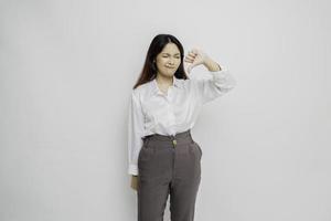 Disappointed Asian woman wearing white shirt gives thumbs down hand gesture of approval, isolated by white background photo