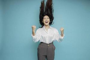 una joven asiática con una expresión feliz y exitosa que usa pantalones blanco aislada de fondo azul foto