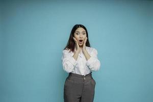 Shocked Asian woman wearing white shirt and looking at the camera, isolated by blue background photo