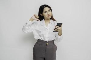 A disappointed Asian woman wearing white shirt gives thumbs down hand gesture of disapproval, isolated by white background photo