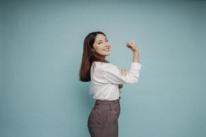 Excited Asian woman wearing a white shirt showing strong gesture by lifting her arms and muscles smiling proudly photo