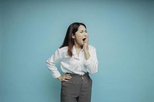 Portrait of sleepy attractive Asian woman wearing a white shirt, feeling tired after night without sleep, yawning, covering opened mouth with palm photo