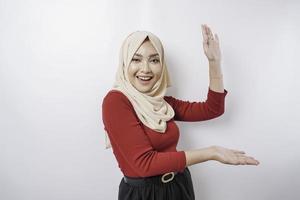 Excited Asian woman wearing hijab pointing at the copy space beside her, isolated by white background photo