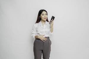 Photo of a hungry excited young woman holding her phone and wondering what to order yummy food isolated on white color background