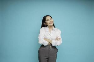 Portrait of a confident smiling Asian woman wearing white shirt standing with arms folded and looking at the camera isolated over blue background photo