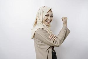 emocionada mujer musulmana asiática usando un hiyab mostrando un gesto fuerte levantando sus brazos y músculos sonriendo con orgullo foto