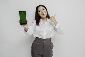 Excited Asian woman wearing white shirt gives thumbs up hand gesture of approval while showing copy space on her phone photo