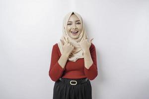 Excited Asian woman wearing a hijab gives thumbs up hand gesture of approval, isolated by white background photo