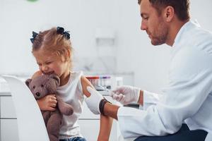 muestra de sangre. niña con su osito de peluche está en la clínica con el médico foto