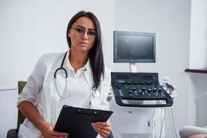 retrato de un médico obstetra que se sienta en la sala de la clínica con un dispositivo de ultrasonido