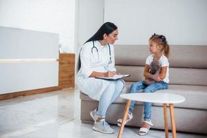 doctora con bloc de notas se sienta en la clínica con una niña