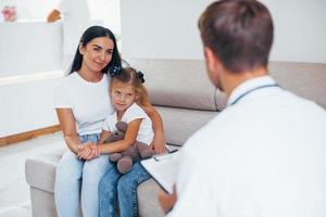 Mother with her cute daughter is visiting clinic. Listening to the doctor photo