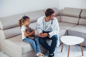 Male doctor in white uniform sits in the clinic with little girl photo