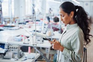 Woman dressmaker stands in the factory with phone in hands photo