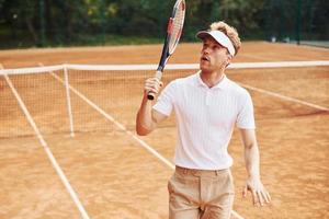 Celebrating victory. Young tennis player in sportive clothes is on the court outdoors photo