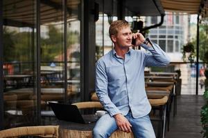 tener una conversación por teléfono. vista frontal del tipo que está en un café moderno con su computadora portátil durante el día foto