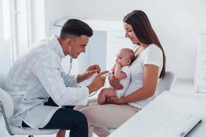 con la ayuda de la madre. el joven pediatra está con un bebé en la clínica durante el día foto