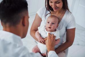 With mother's help. Young pediatrician is with little baby in the clinic at daytime photo