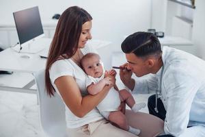 con la ayuda de la madre. el joven pediatra está con un bebé en la clínica durante el día foto